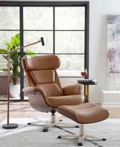 an office chair and footstool in front of a large window with a potted plant