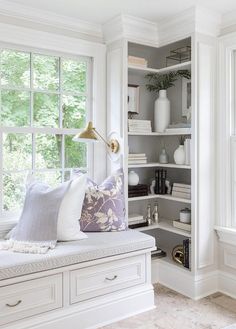 a window seat with pillows on it in front of a book shelf filled with books