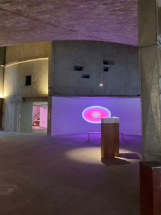 an empty room with a purple light on the wall and a round table in the middle