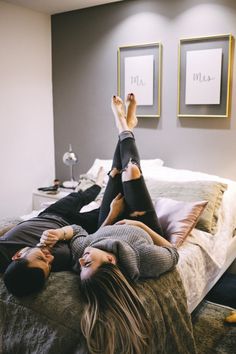 two people laying on a bed with their feet up in the air and one person wearing black