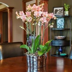 pink flowers in a metal basket on a wooden table with black leather chairs around it