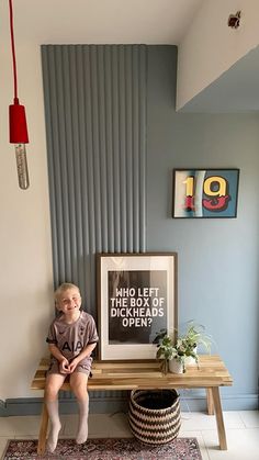 a young boy sitting on a bench in front of a wall with pictures and plants