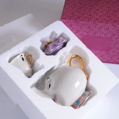 an open box with two teapots in the shape of elephants and other items