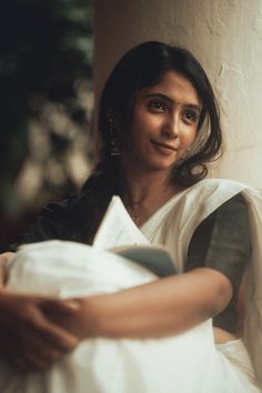 a woman sitting on a couch with her arm around a pillow and looking at the camera