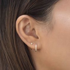 a woman's ear is shown with two small diamond hoop earrings on top of it