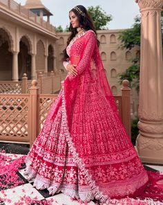 a woman in a pink and white lehenga with flowers on the ground behind her