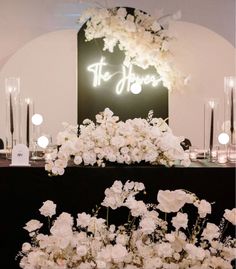 white flowers and candles on a black table with a neon sign above it that says st john