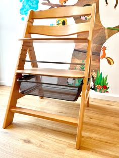 a child's wooden rocking chair in front of a wall with an animal mural