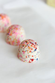 three chocolate covered candies with sprinkles sitting on a white tablecloth