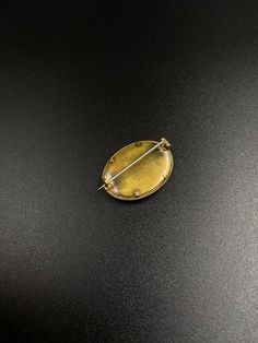 a gold brooch with a pin in the middle on a black surface, close up