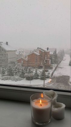 two candles sitting on a window sill in front of a snowy street