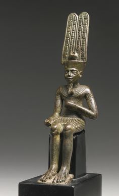 an ancient statue sitting on top of a black block with a gold headdress