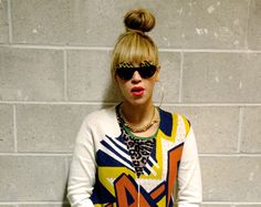 a woman wearing sunglasses and a sweater with an animal print on the front, standing in front of a brick wall