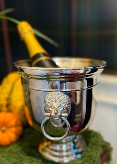 a metal bowl with a lion head on the front and handles is sitting next to some oranges