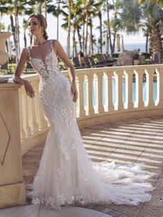 a woman in a wedding dress standing on a balcony next to a pool and palm trees