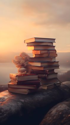 a stack of books sitting on top of a rock next to the ocean at sunset