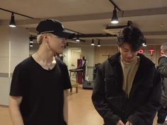 two young men standing next to each other in a room with wooden floors and lights