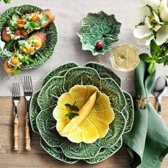 a table topped with green plates and silverware next to flowers on top of a wooden table