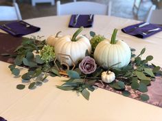 white pumpkins and greenery on a table with purple napkins at the end