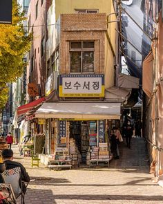 people are sitting on benches in the middle of an alleyway with buildings and shops