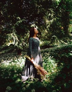 a woman standing in the grass holding a broom and looking up into the sky with her eyes closed