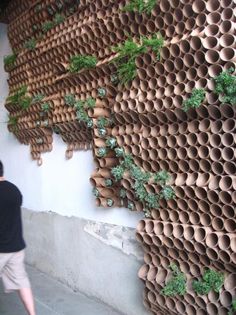 a man walking past a wall made out of clay pipes and plants on the side