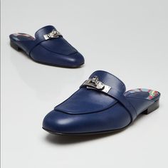 a pair of blue shoes with silver buckles on the front and back, sitting on a white surface