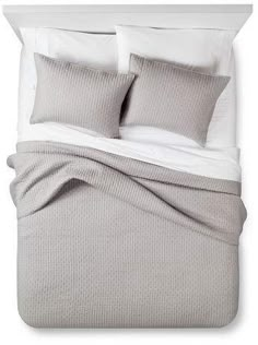 a bed with grey sheets and white pillows