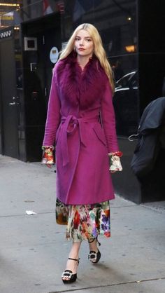 a woman in a purple coat is walking down the street with her hand on her hip