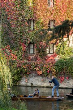 two people in a boat on a river with ivy covered buildings behind them and one person holding a paddle