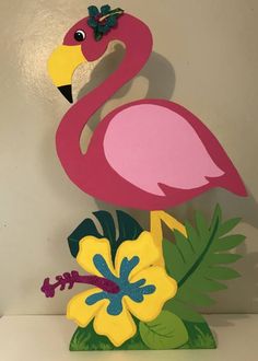 a pink flamingo standing on top of a lush green leafy plant next to a white wall