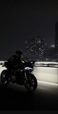 a person riding a motorcycle on a highway at night with city lights in the background