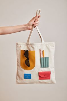 a hand holding a canvas bag with various items on it and a pair of scissors