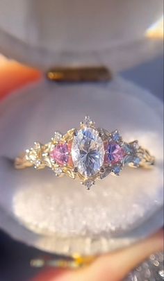 an engagement ring with three different colored stones on the front and side, sitting in a box