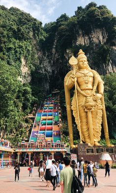 people are walking around in front of a large golden statue on the side of a mountain