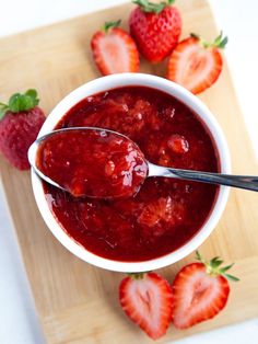 a bowl of strawberry jam with two spoons in it and strawberries on the side