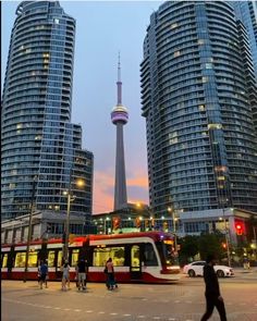 people are walking around in front of some tall buildings at dusk with the sky tower in the background