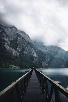 a pier with mountains in the background and cloudy skies above it on a mountain lake