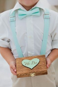 a little boy wearing a bow tie and suspenders holding a wooden sign with the word do we love you