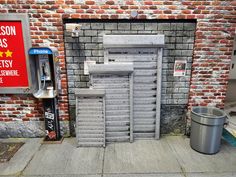 an old fashioned phone booth next to a trash can on the side of a brick building