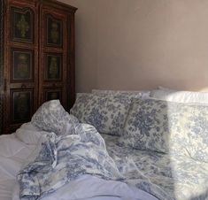 an unmade bed with blue and white comforter in a bedroom next to a wooden cabinet