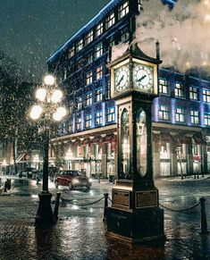 a clock tower sitting in the middle of a street at night with steam pouring out of it