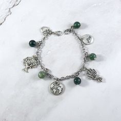 a bracelet with charms on it sitting on top of a white marble countertop next to a tree