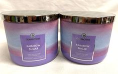 two purple candles are sitting side by side on a white tablecloth, one has a silver lid and the other has a rainbow sugar jar