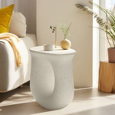 a white table sitting on top of a wooden floor next to a couch and potted plant