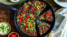 a skillet filled with corn and vegetables on top of a wooden table next to other dishes