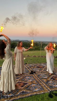 three women holding torches in their hands while standing on top of a rug with grass