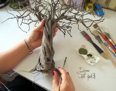 a woman is making a tree out of branches with scissors and paintbrushes on the table