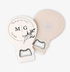 two white bottle openers with the letter m g on each one and a heart shaped hole in the middle