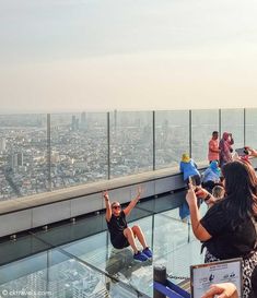 people sitting and standing on the edge of a building looking out at cityscape